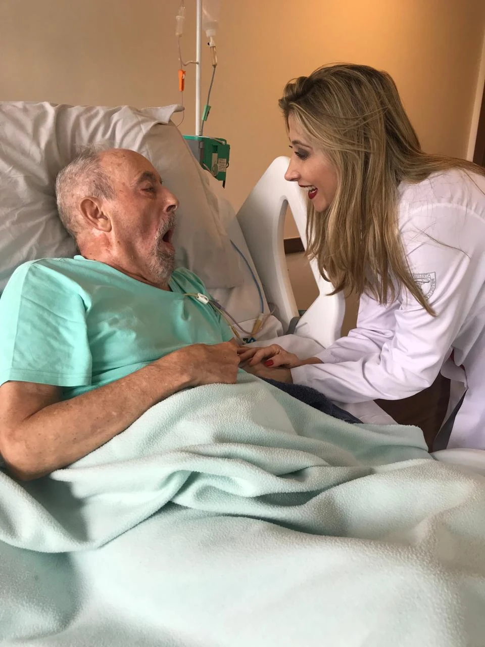 Dra. Juliana Venites em atendimento clínico a um paciente idoso em leito hospitalar